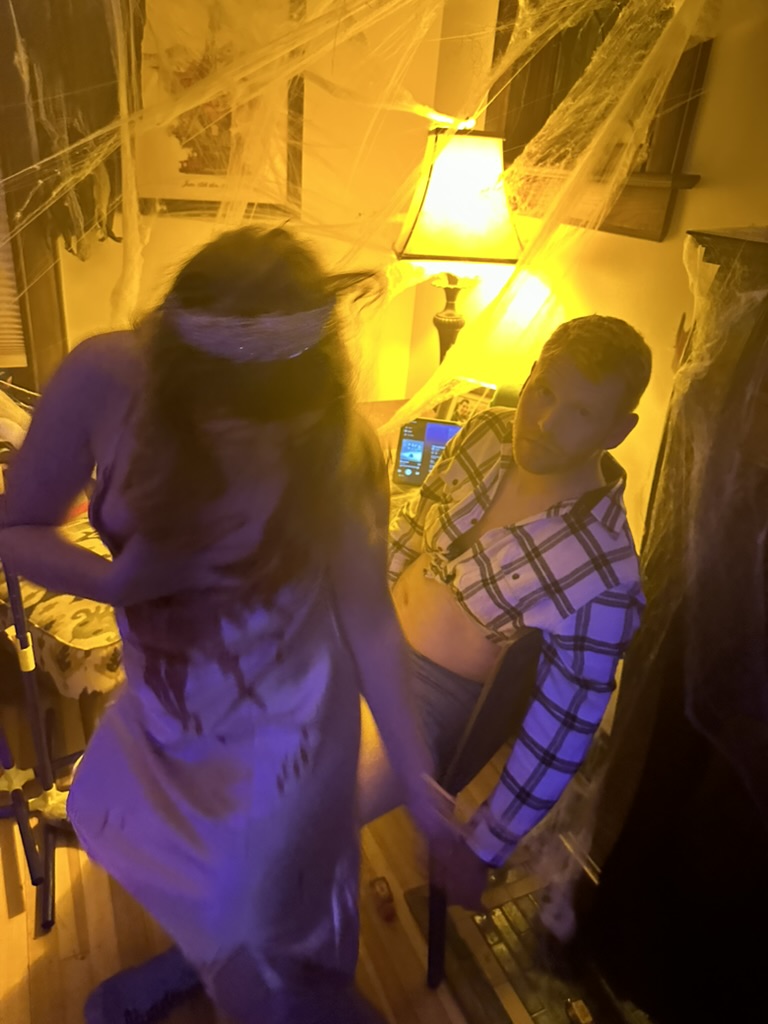 Two costumed guests on an exercise bike surrounded by cobwebs and lamp light