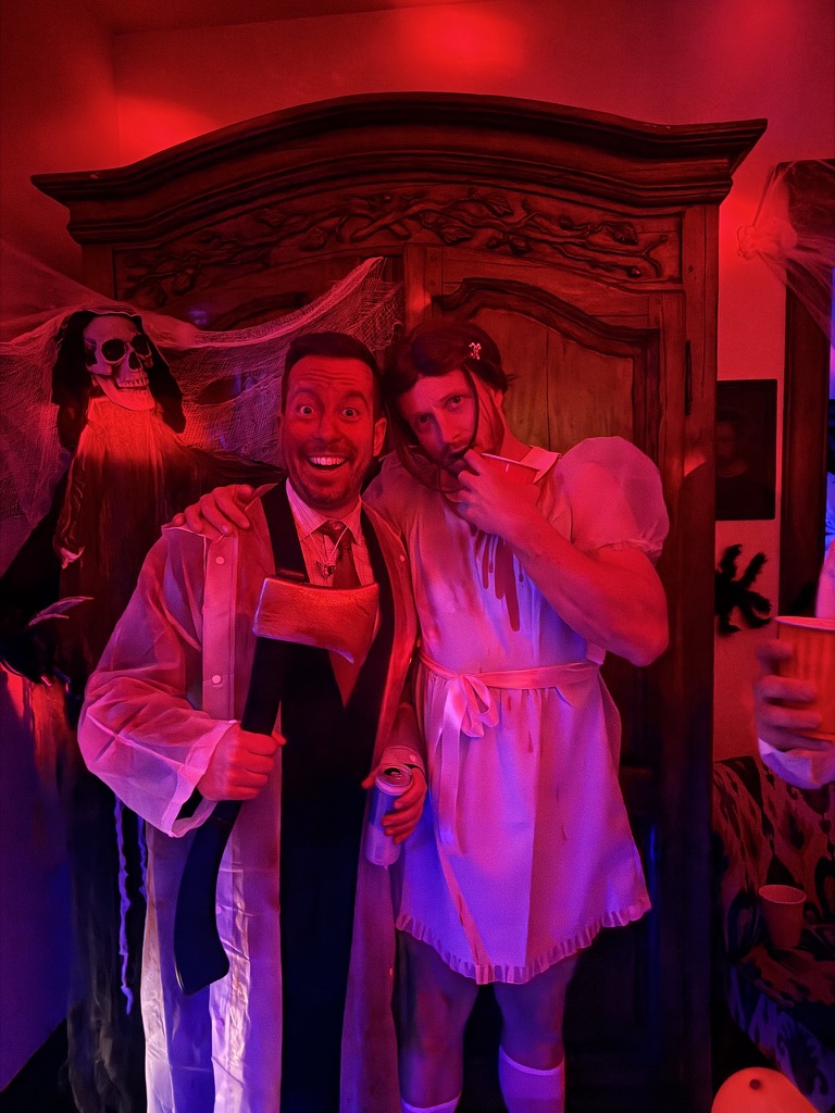 Two guests in full costume — an axe-wielding businessman and a bearded man in a bloody nightgown