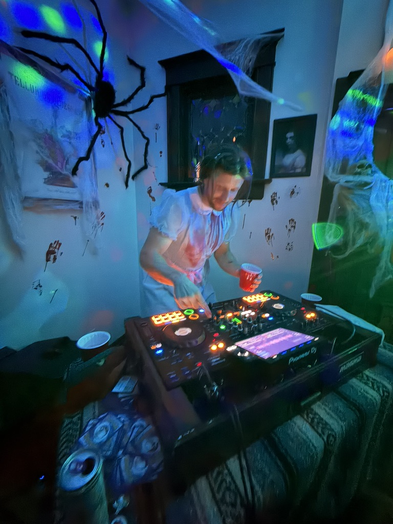 The DJ playing a live set on Pioneer decks surrounded by cobwebs and a giant spider