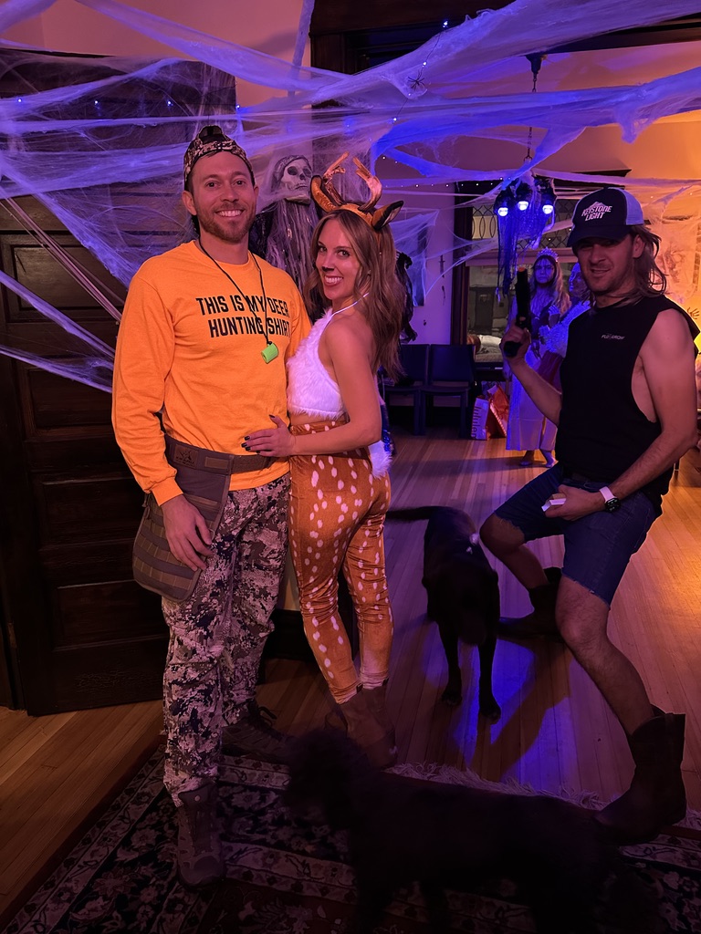 Three guests dressed as a deer hunter, a deer, and a mullet cowboy, with two dogs