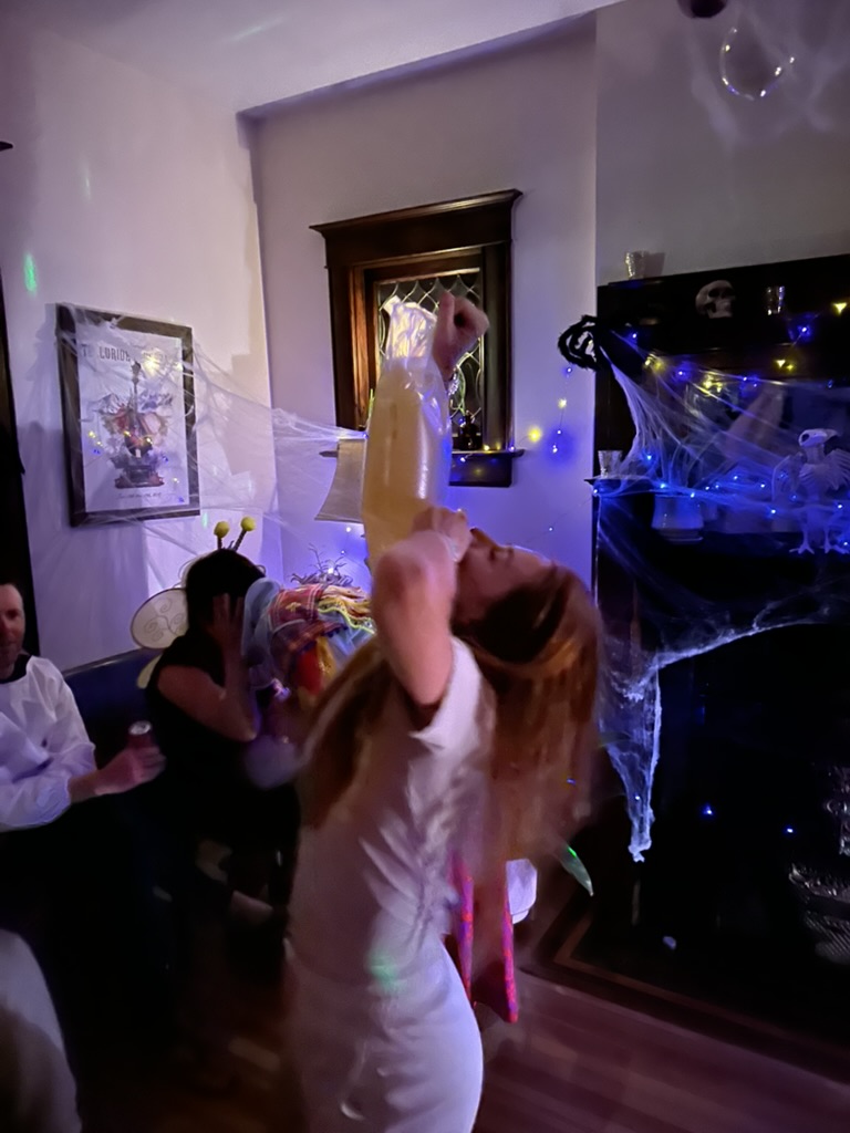 Guest in a white angel costume chugging from a large jug by the fireplace