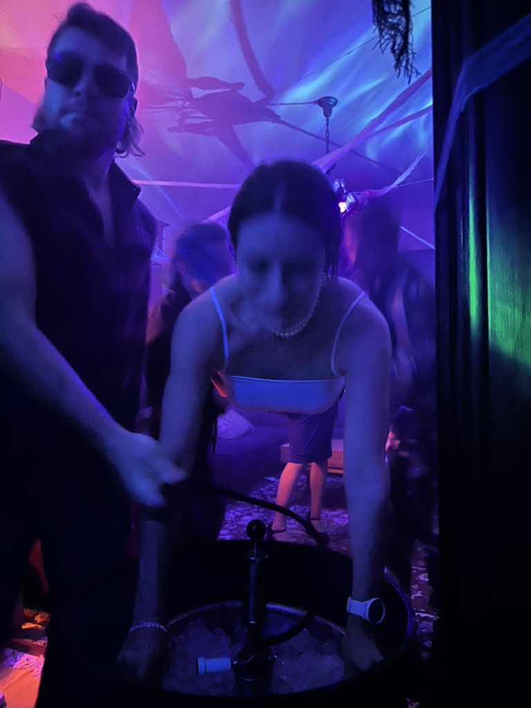 Two guests in costume working the keg tap over a bucket of ice under purple party lights