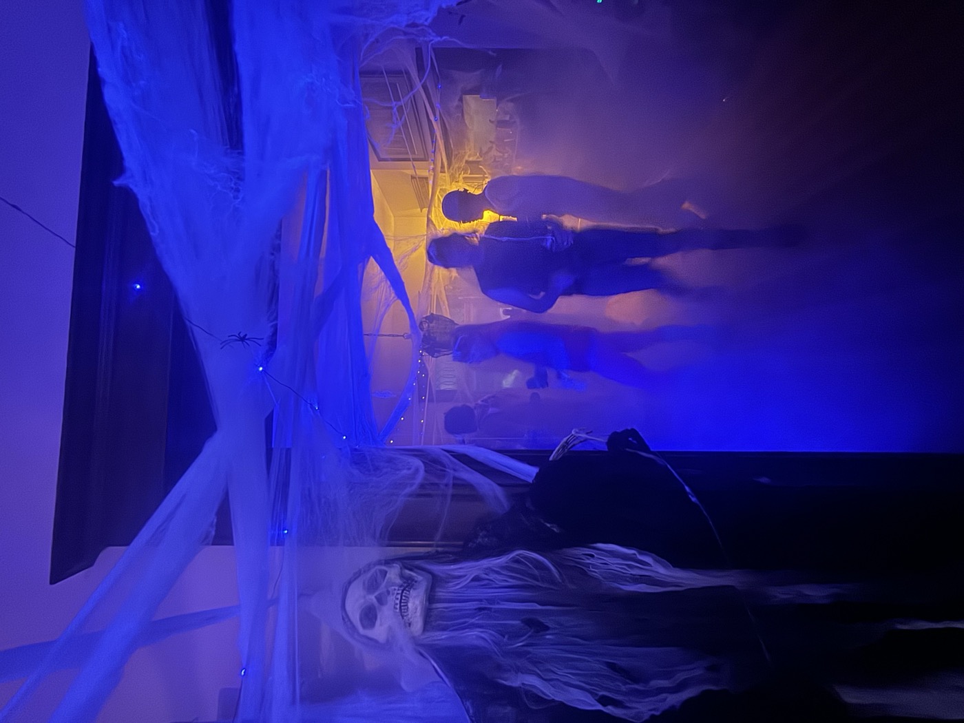 A grim-reaper decoration looms as guests move through a blue-lit, fog-filled hallway