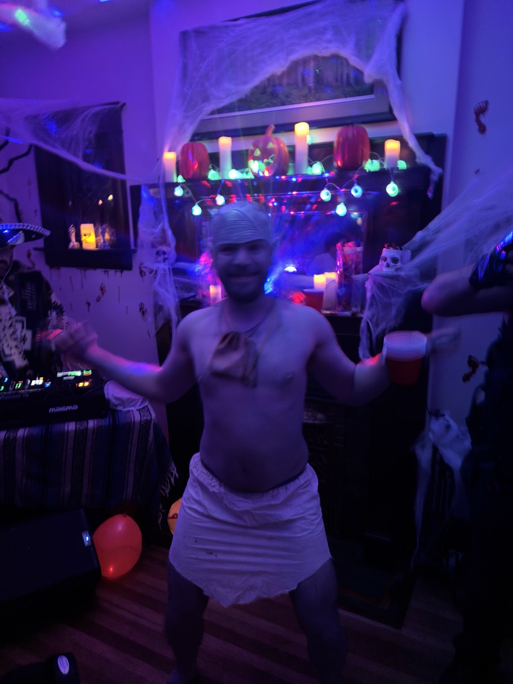A guest in a toga and headband dances with a red cup among candles and cobwebs