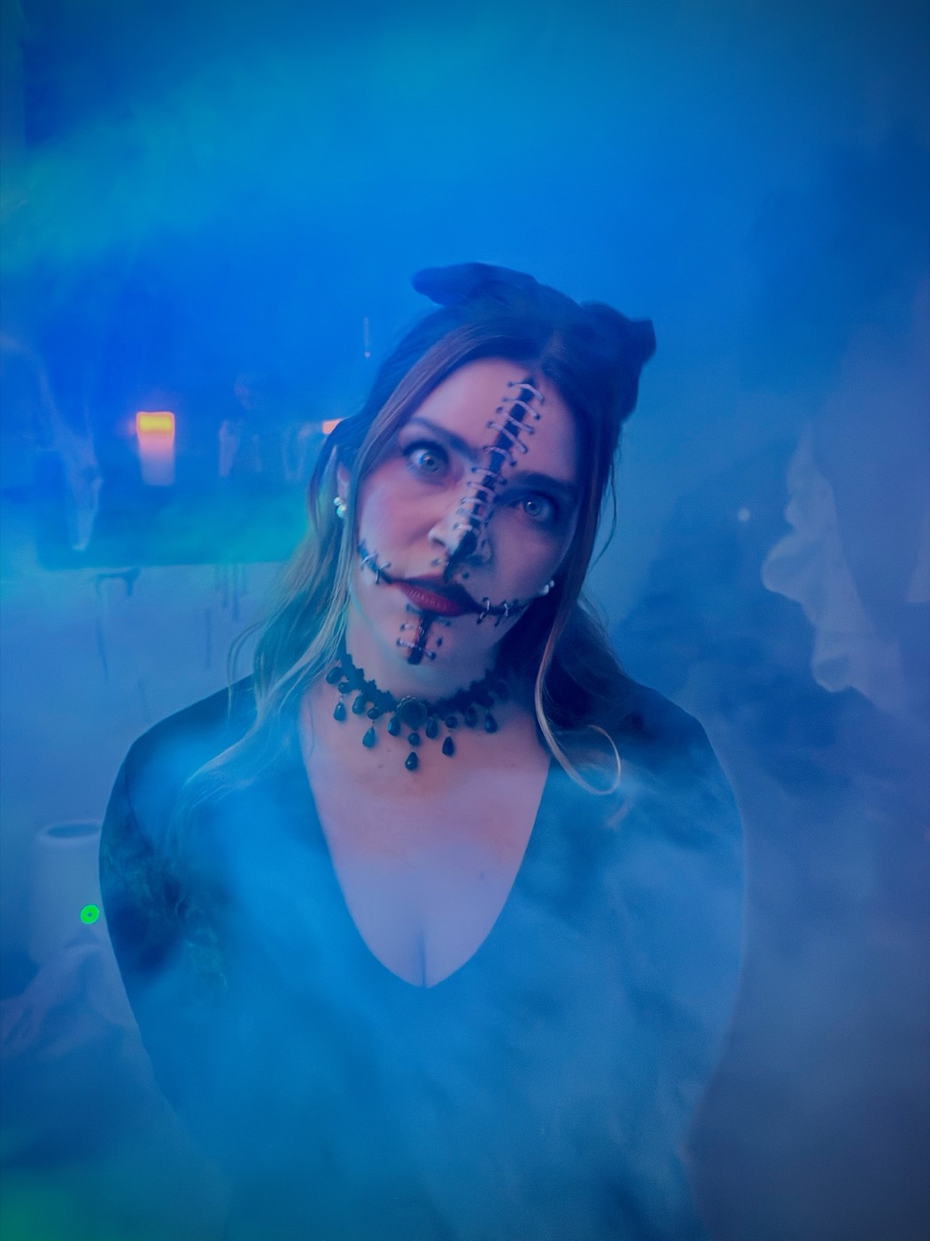 A guest with cracked-porcelain-doll face makeup, cat ears, and a beaded choker in blue smoke
