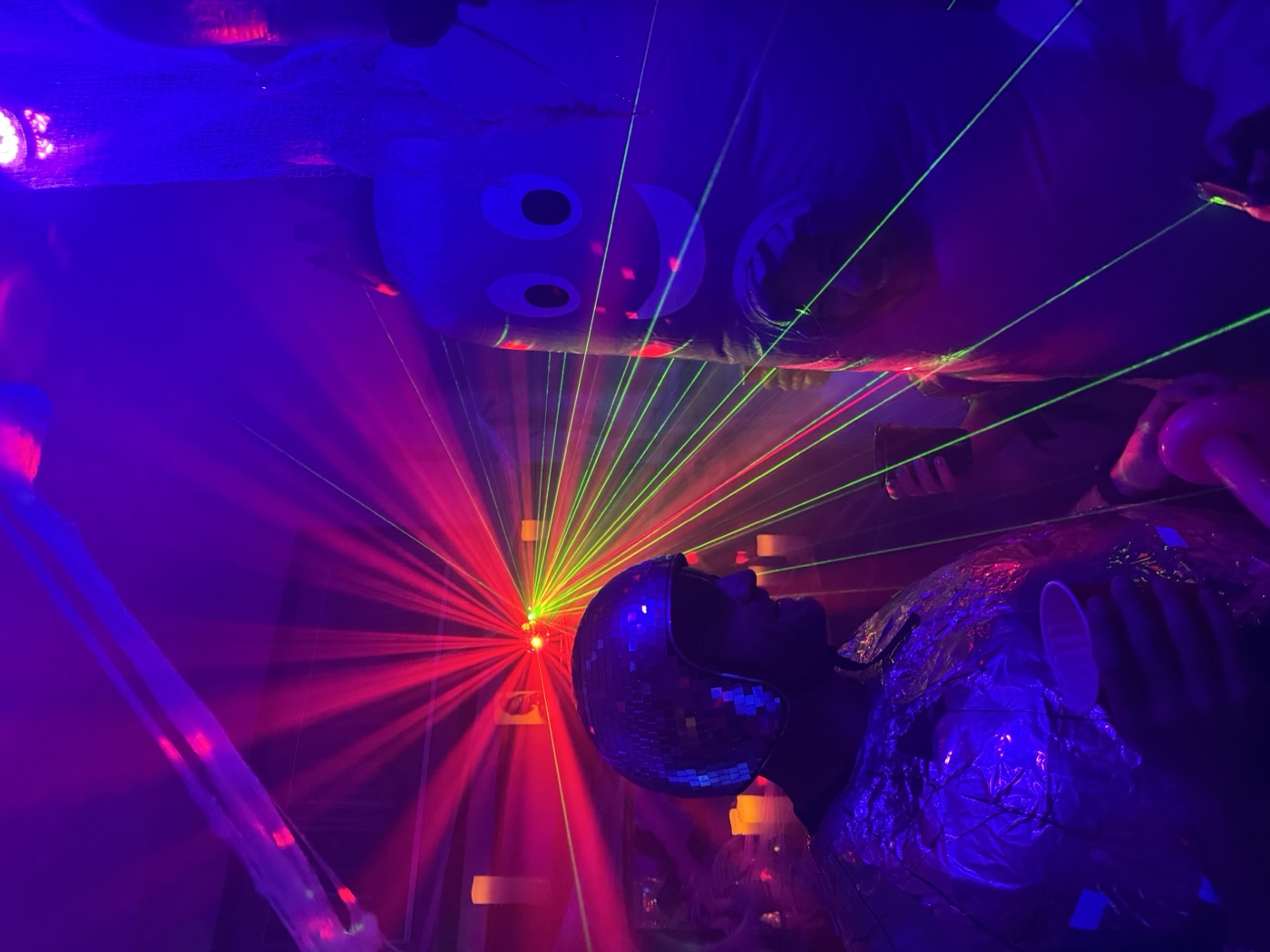 A guest in a mirror-ball helmet faces off with the purple mascot as red lasers streak between them